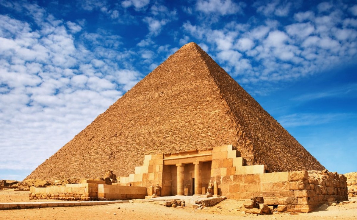 The Great Pyramid of Giza under a bright blue sky with scattered clouds.