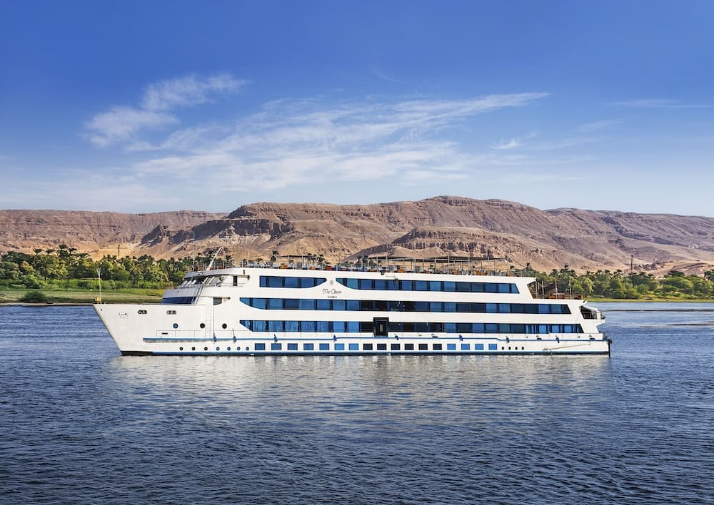 A modern cruise ship sailing on the Nile with the backdrop of the Egyptian landscape.