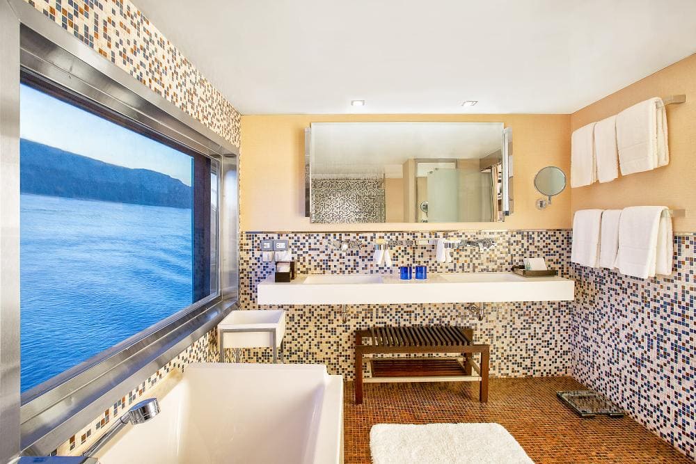 A bathroom with a large window overlooking a tranquil sea, featuring a mosaic tile design