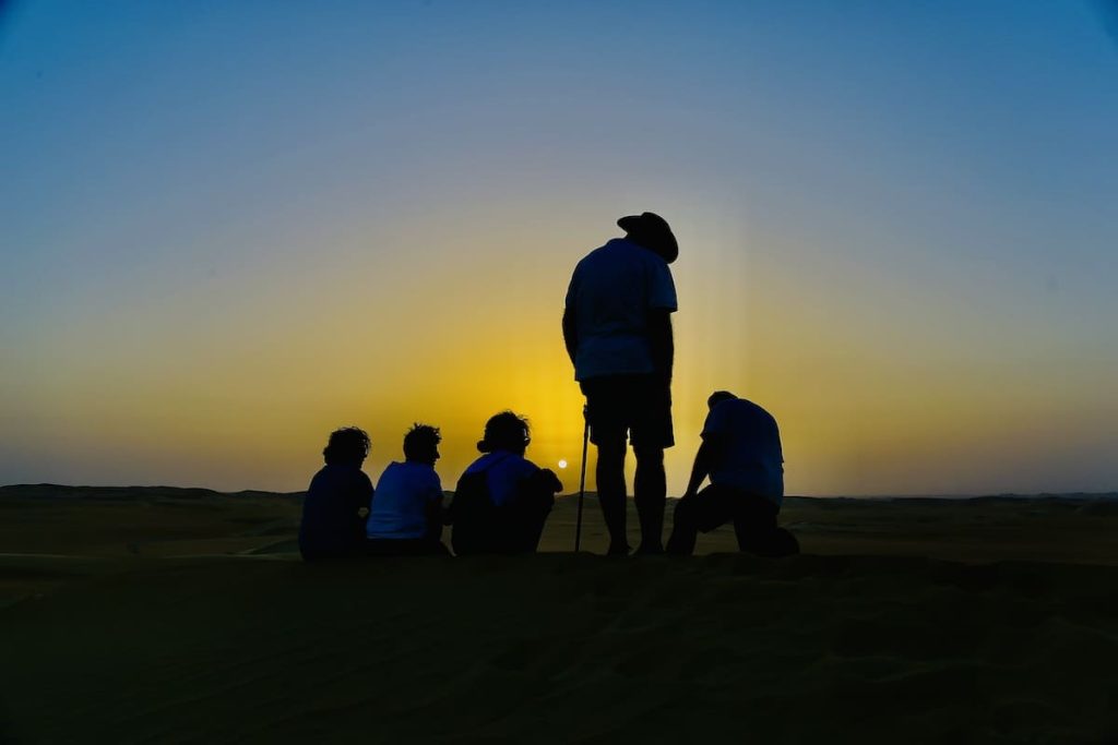 A group of people silhouetted against a vivid sunset sky in the desert.