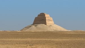 The Meidum Pyramid standing isolated in the Egyptian desert under a clear sky.