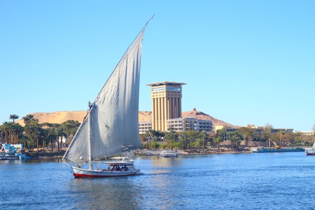 Traditional felucca sailing on the Nile with Aswan cityscape in the background.