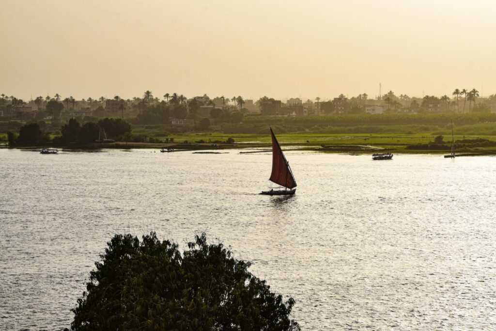 A single sailboat on the Nile at sunset, with the sun reflecting off the water.