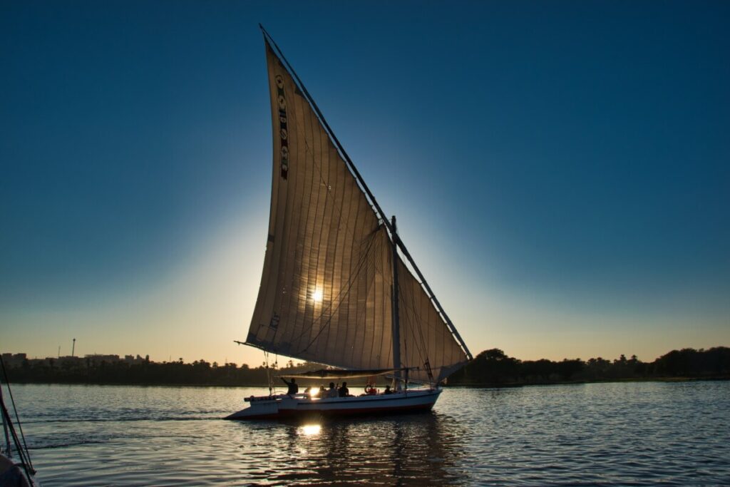 A felucca sailing on the Nile River at sunset, with the sun peeking through the sail.