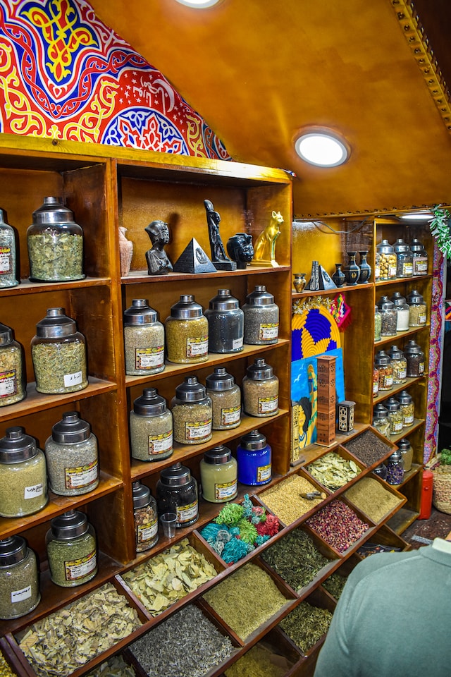 Glass jars and wooden containers filled with assorted spices on shelves in a cozy shop interior.