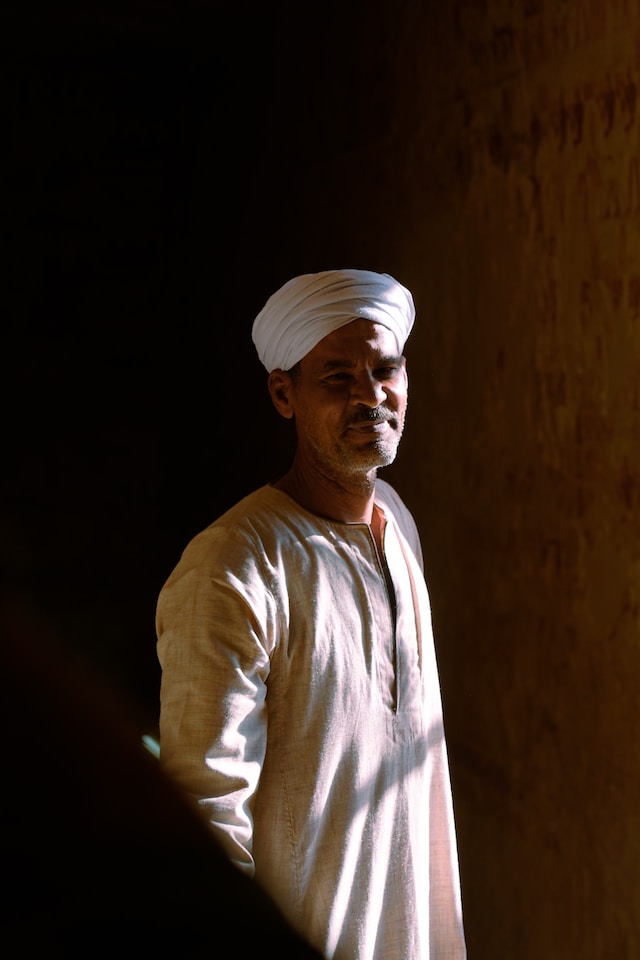 A man in traditional attire with a white turban illuminated by natural light.