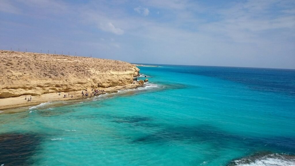 A serene beach with turquoise waters and a rugged coastline under a clear sky.