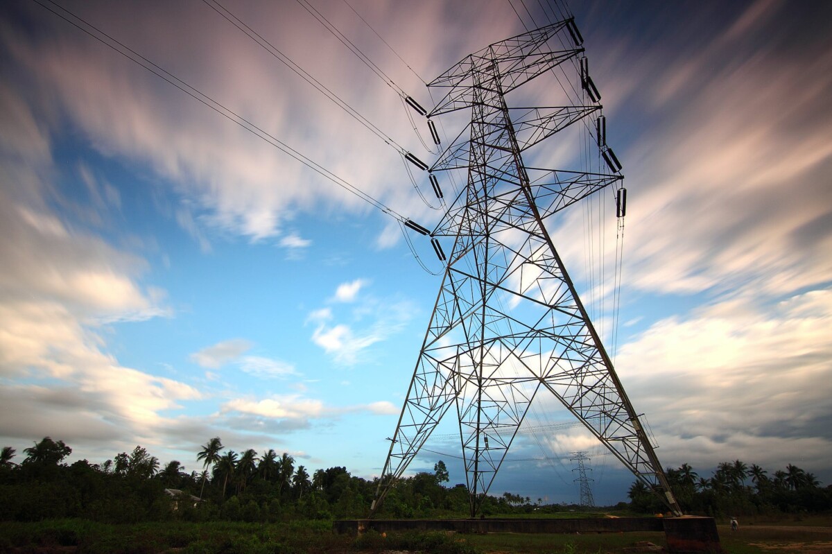 A towering electricity pylon against a dynamic sky with fast-moving clouds.