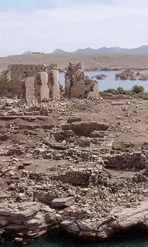 Ancient stone ruins of Qasr Ibrim with a backdrop of a lake and distant mountains under a clear sky.