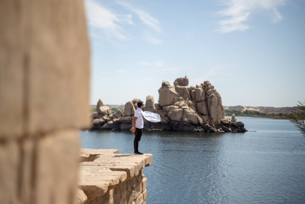 A person standing on the edge of a stone platform overlooking the Nile River and rock formations.