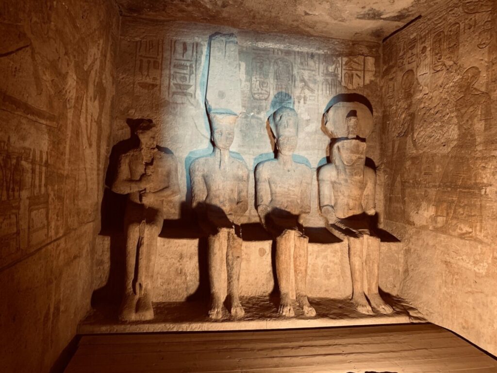 Four ancient Egyptian statues carved into rock at the Abu Simbel temple, with hieroglyphics on the walls.