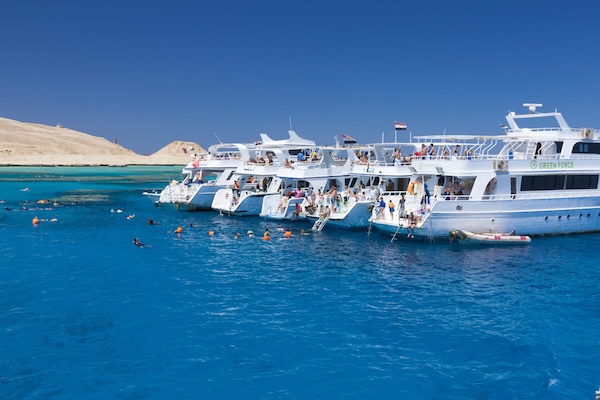 Tourists enjoying snorkeling in crystal-clear blue waters near white excursion boats under a bright sky.
