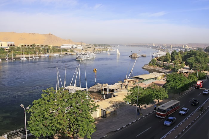 Panoramic view of Aswan city with the Nile River, feluccas, and a bustling street.