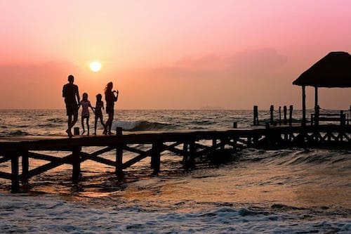 A family enjoying a sunset on a wooden pier by the beach.