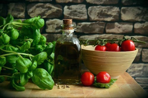 A still life setup with fresh basil, ripe tomatoes, and a bottle of olive oil on a wooden board