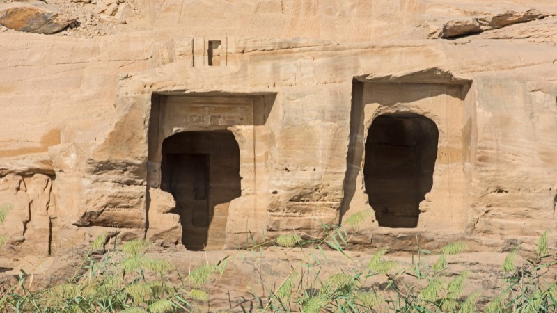 "Ancient Egyptian tombs cut into a rocky hillside by the Nile."