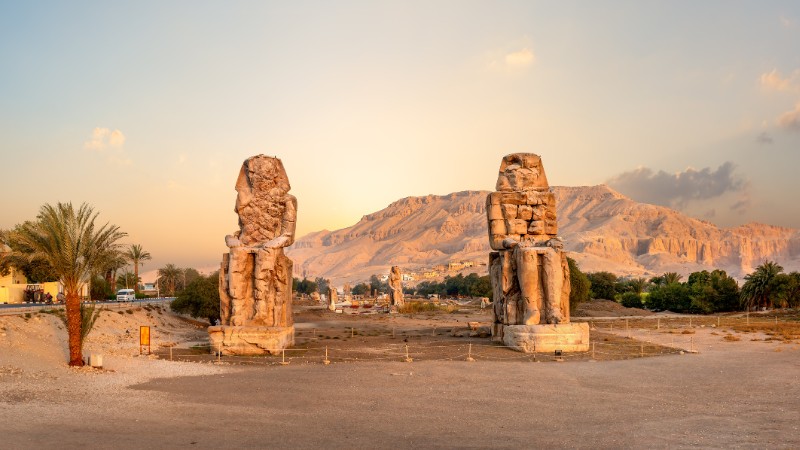 "Two massive stone statues, the Colossi of Memnon, during sunrise."