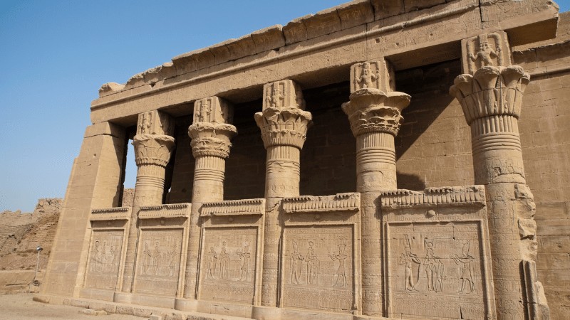 "The ancient colonnade of Philae temple with carved hieroglyphs, under a clear blue sky."