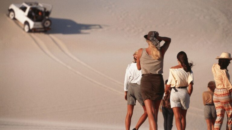 "People watching a vehicle ascending a desert dune."