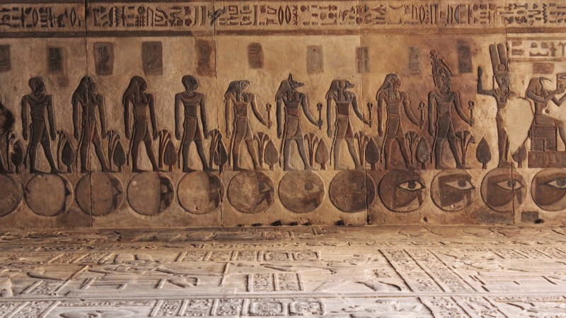 "Relief of hieroglyphic carvings depicting figures and symbols on a wall in an Egyptian temple."