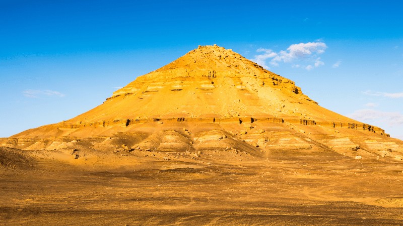 "A towering pyramid-shaped mountain under a clear blue sky in a desert landscape."