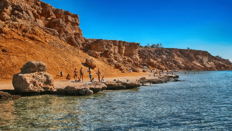 Visitors enjoy a sunny day on the rocky beaches of Sharm El Sheikh with clear blue waters in the foreground