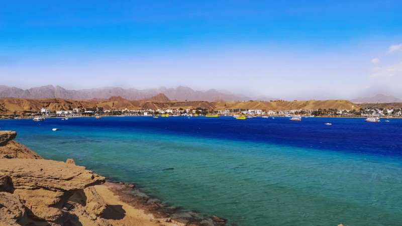 Clear blue waters along the coastline of Sharm El Sheikh with mountainous backdrop and boats docked near the shore