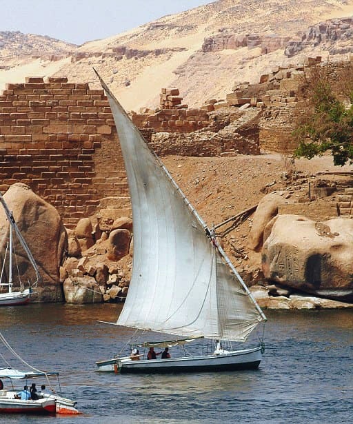 View of Elephantine Island on the Nile River with a felucca in the foreground.