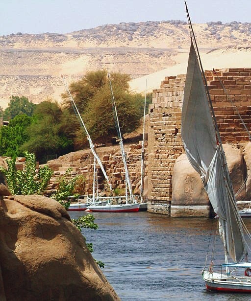 A traditional felucca sailing near the sandy shores of Elephantine Island on the Nile River.