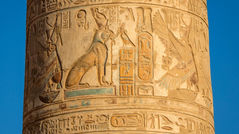 "Close-up of an ancient Egyptian column with hieroglyphic carvings depicting gods and symbolic inscriptions."