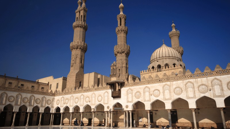 Exterior view of Al-Azhar Mosque with its iconic minarets and dome under a clear blue sky."
