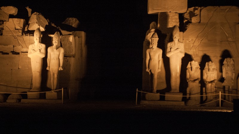 "Statues of ancient Egyptian figures lit up at night."