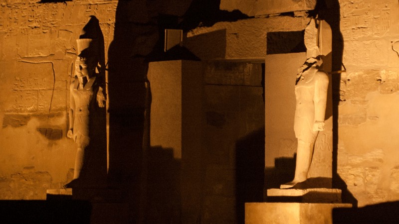 "Statues illuminated at night within Karnak Temple in Luxor, Egypt, casting long shadows on ancient hieroglyph-covered walls."