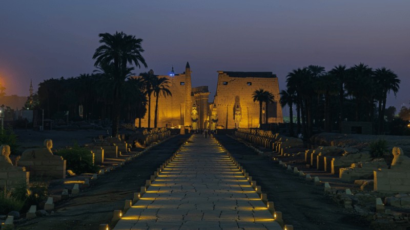 The Karnak Temple illuminated at dusk with a pathway lined by sphinx statues leading to the entrance