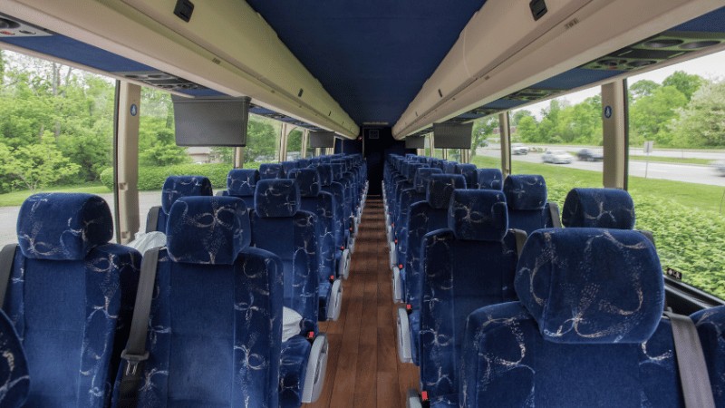 "Interior view of an empty bus with blue upholstered seats and a wooden floor."