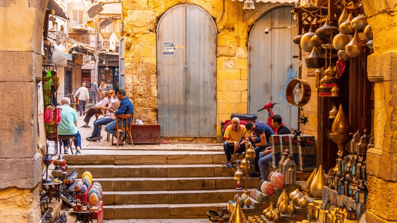 "A vibrant street scene at a market with people, brassware on display, and architectural details in the Middle East."