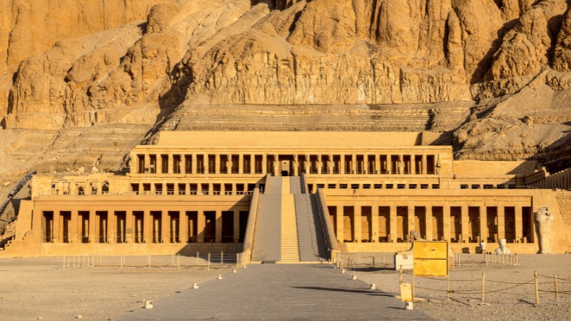 "Ancient Temple of Queen Hatshepsut with towering cliffs in the background, under a clear sky."
