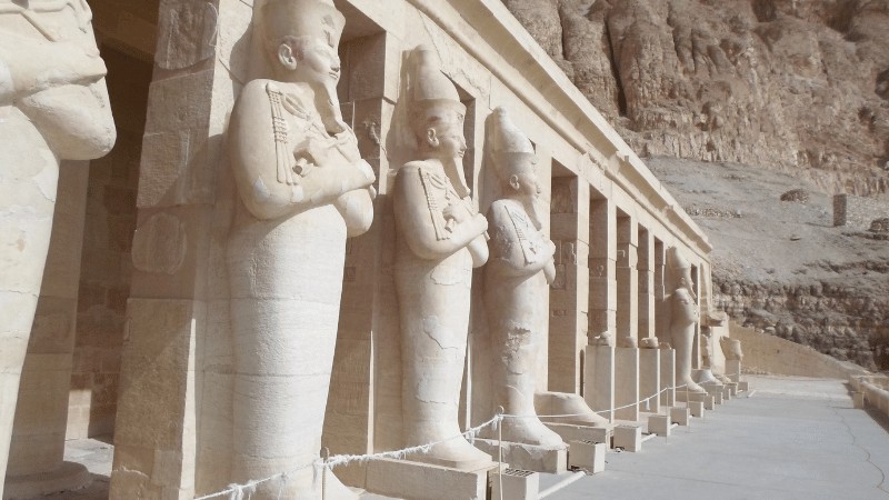 "Statues of pharaohs standing guard at the entrance of an ancient Egyptian temple carved into a rock face."