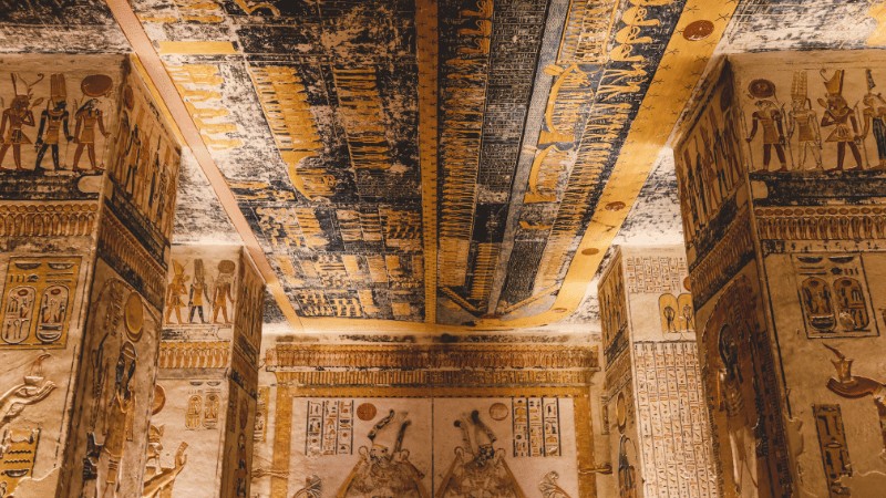 "Intricately decorated ceiling and walls of an Egyptian tomb with hieroglyphs and depictions of deities and pharaohs."