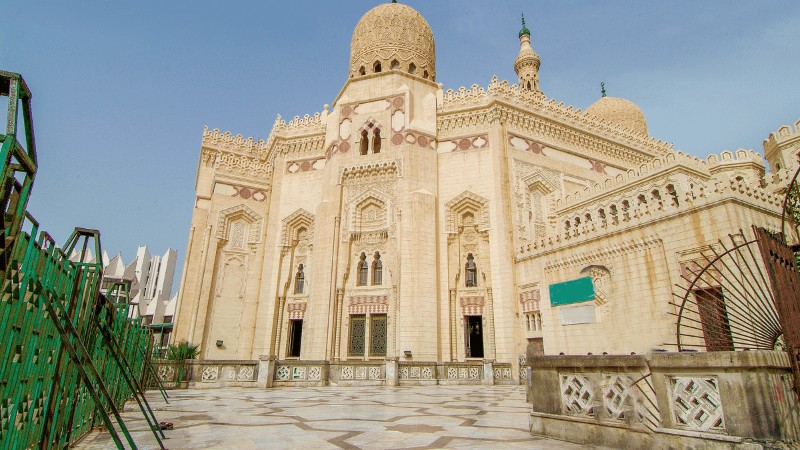 "Wide-angle view of a grand mosque with ornate detailing and a clear blue sky."