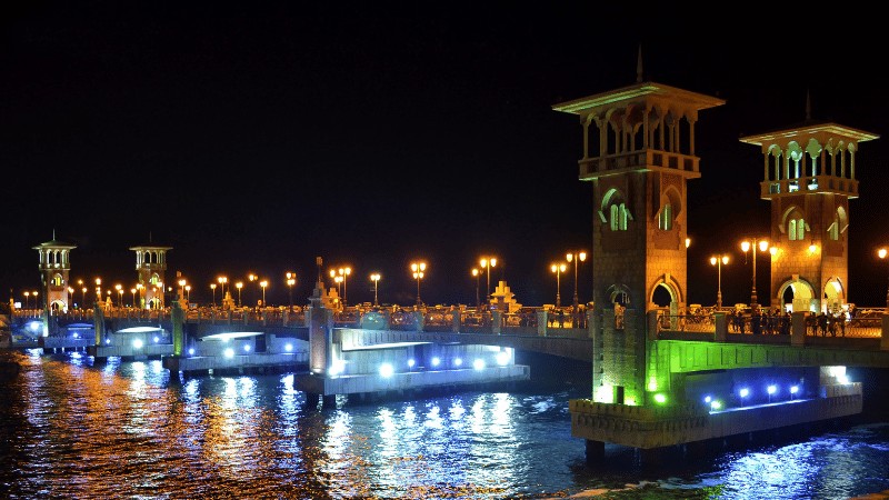 "An illuminated bridge with traditional architectural towers and lamp posts reflecting on the water at night."
