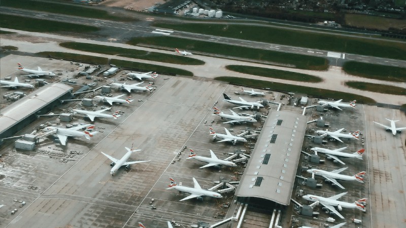 "Overhead view of multiple airplanes parked at airport gates with terminal buildings in the foreground."