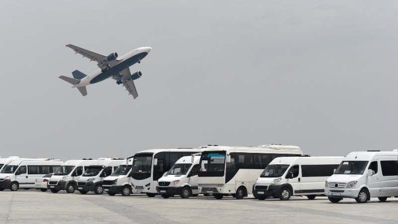"An airplane taking off above a line of parked shuttle buses at an airport."