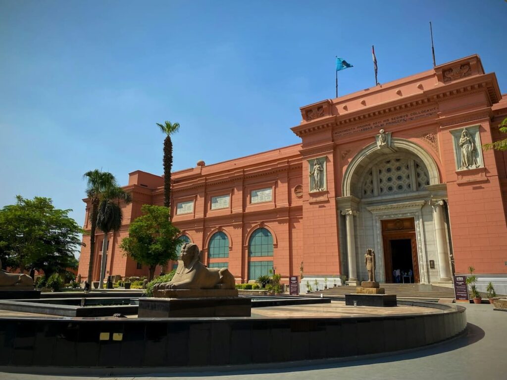 Front entrance of the Egyptian Museum in Cairo, with Sphinx statues and a palm tree under a clear blue sky