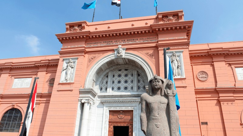 "Front view of the Egyptian Museum with a statue and flags under a clear sky."