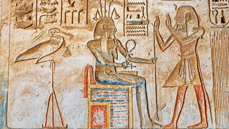 Ancient Egyptian hieroglyphs depicting a seated pharaoh and deities.