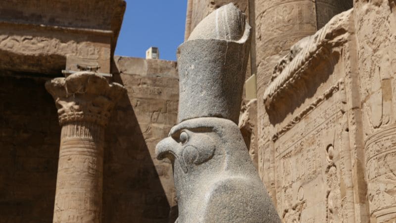 A granite statue of a falcon-headed Egyptian deity in a temple complex.