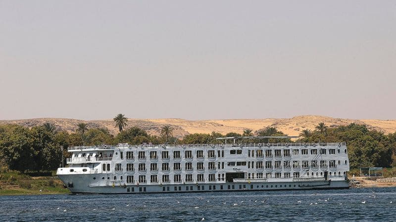 A white cruise ship sailing on the Nile River with desert hills in the background.