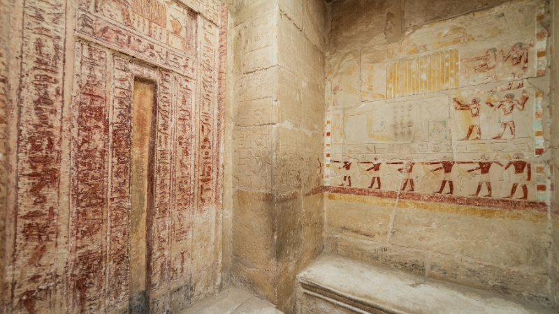 Interior wall of an Egyptian tomb with ancient hieroglyphs and faded paintings.