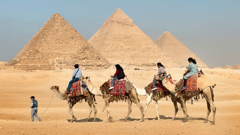 Tourists on a camel ride in front of the Pyramids of Giza.
